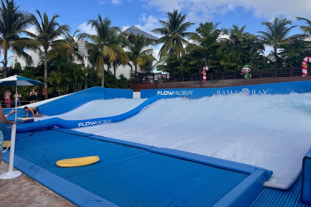 The FlowRider surf simulator at Baha Bay water park, Grand Hyatt Baha Mar, with kids attempting to bodyboard on the artificial wave under a blue sky.