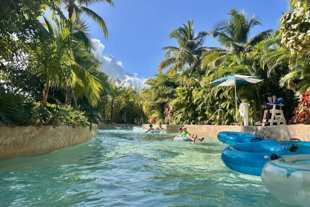 Families floating on tubes through the lush tropical lazy river at Baha Bay water park, Grand Hyatt Baha Mar, surrounded by palm trees and tropical vegetation.