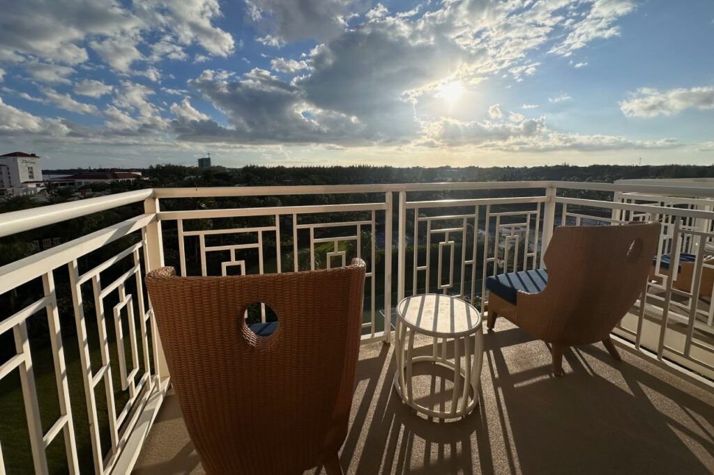 Two wicker chairs and a small side table on a Grand Hyatt Baha Mar room balcony at sunset, with a wide view over Nassau rooftops and palm trees.