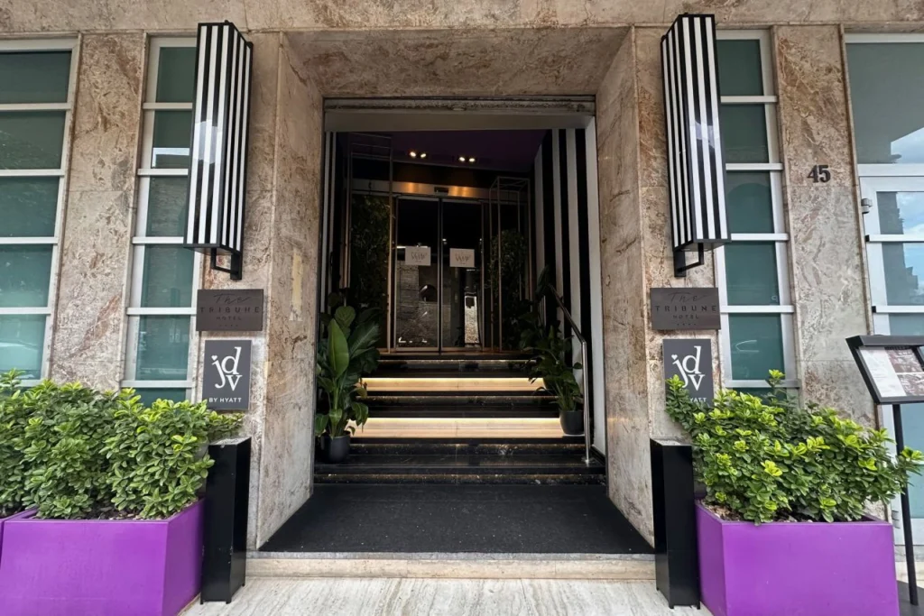 Entrance to The Tribune Hotel, a JdV by Hyatt property in Rome, with marble facade, striped black and white wall sconces, and purple planters flanking the doorway