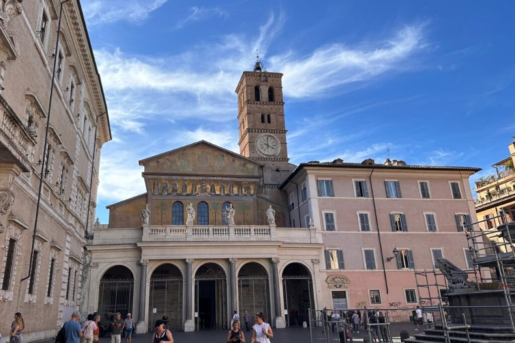 Santa Maria in Trastevere basilica facade with its golden mosaic, clock tower, and Romanesque portico, viewed across the piazza on a sunny day