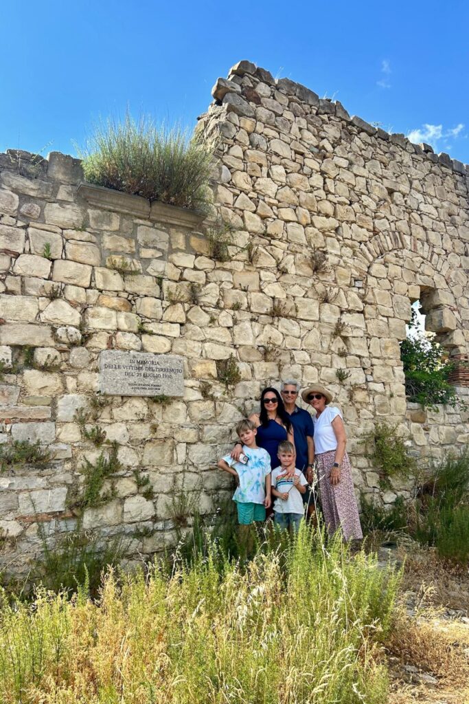 Three generations of the family pose beside the stone memorial wall in Aquilonia honoring the victims of the July 23, 1930 earthquake