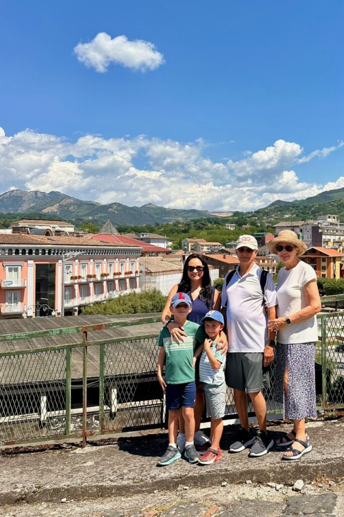 Three generations of the family pose on a bridge overlooking an Avellino town, with terracotta rooftops and mountains in the background