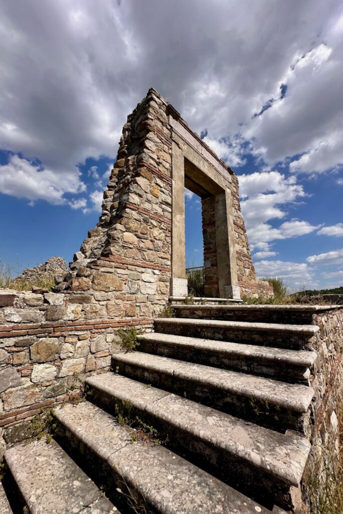 Dramatic upward view of a surviving stone doorway and steps in the ruins of old Aquilonia, framed against a moody cloud-filled sky