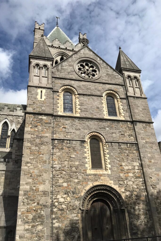 Stone exterior of Christ Church Cathedral in Dublin, Ireland, with a rose window, pointed turrets, and a carved arched doorway.
