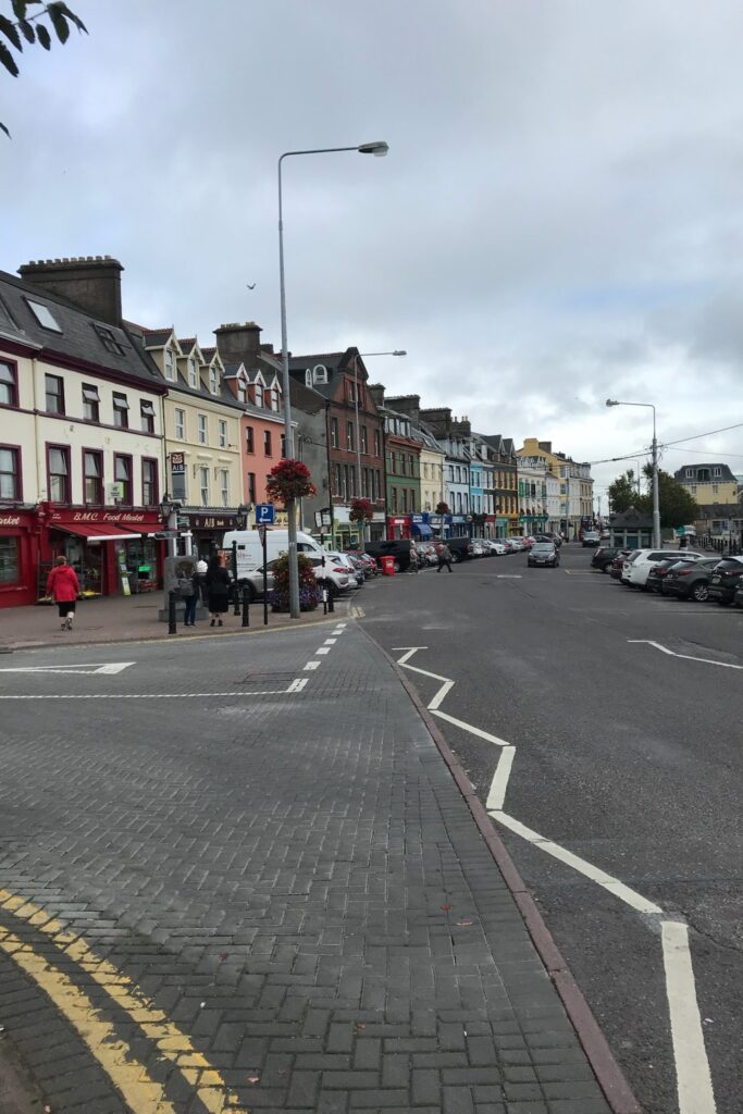 Row of colorful buildings along the waterfront street in Cobh, Ireland, on an overcast day.