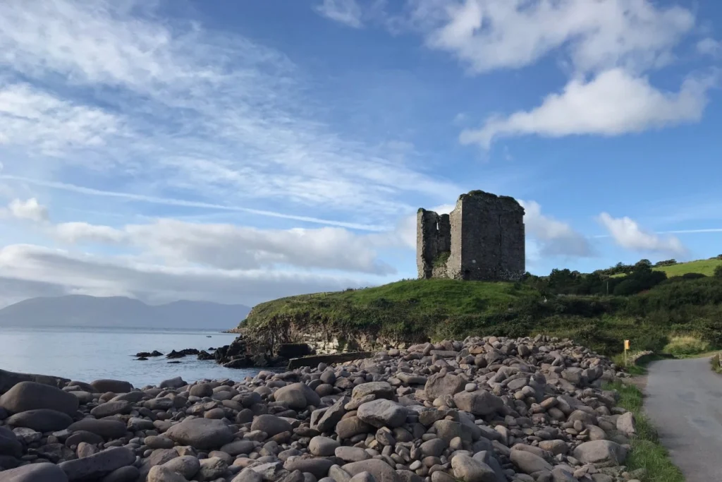 Ruined stone tower house above a rocky beach on the Dingle Peninsula in County Kerry, Ireland.