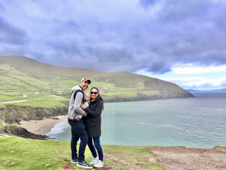 Family of three stands on a cliff overlooking the sea of the Dingle Peninsula Ireland