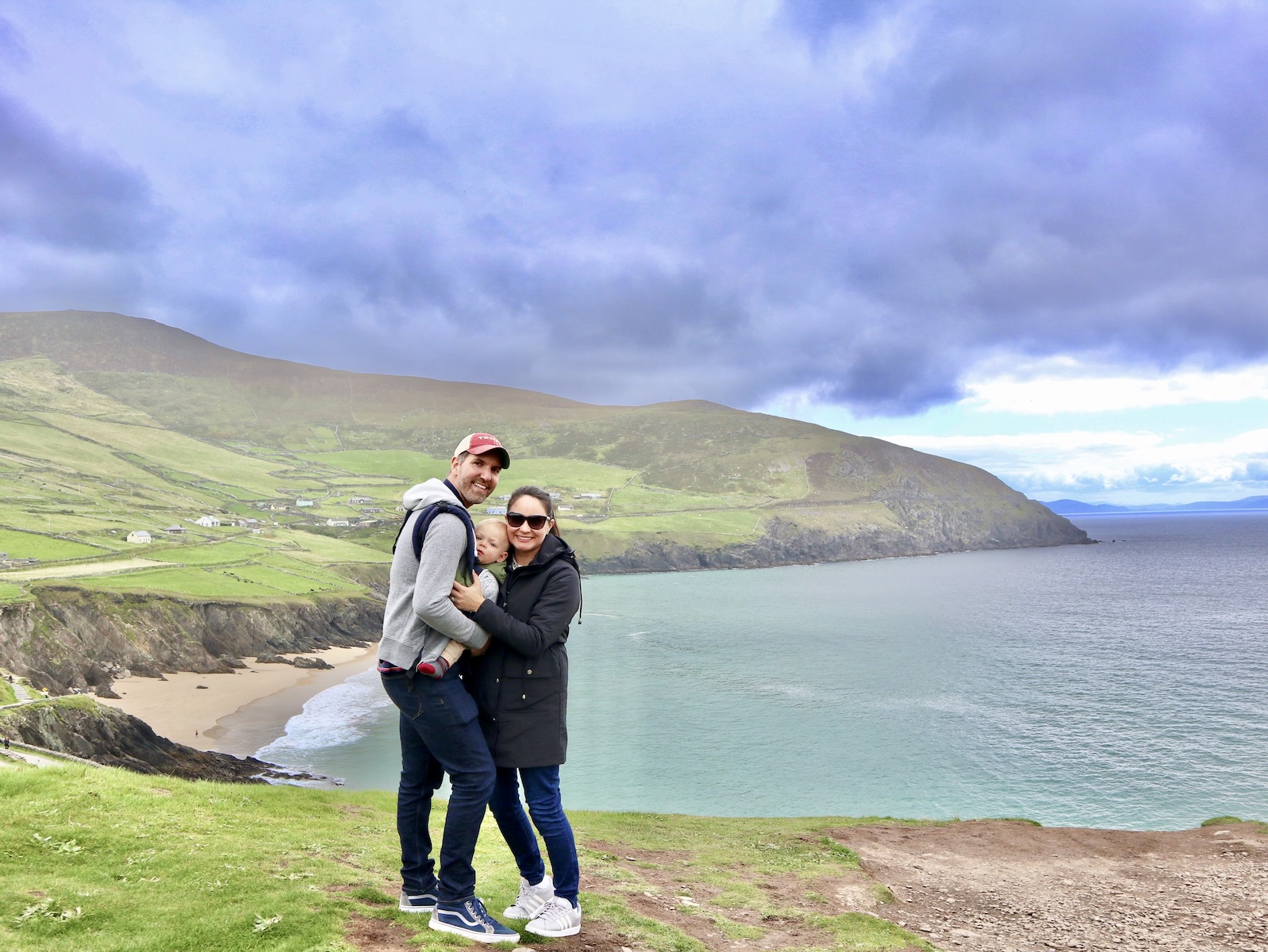 Family of three stands on a cliff overlooking the sea of the Dingle Peninsula Ireland