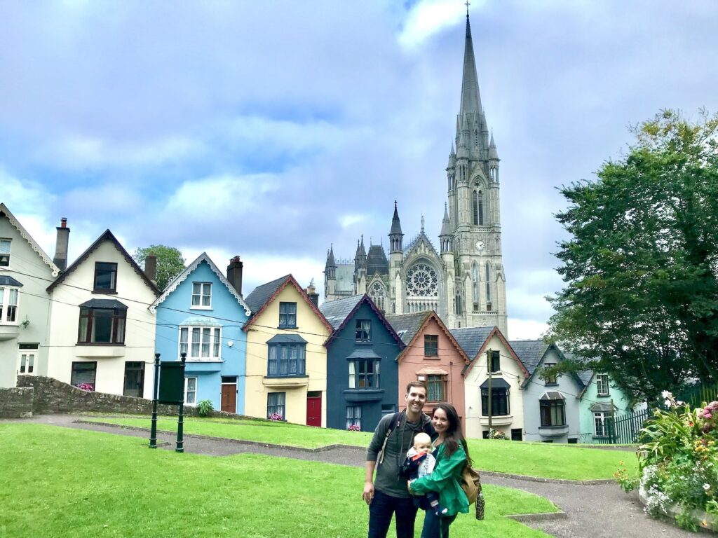 Family of three stands in front of the colorful deck of cards houses and cathedral in Cobh Ireland