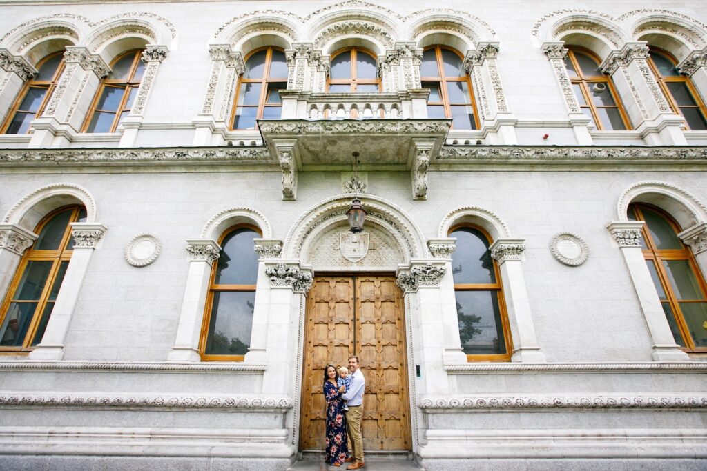 Family of three stands in front of a building at Trinity College Ireland