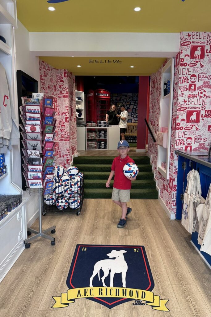 Young boy holding a football inside the Ted Lasso Store in Richmond, standing on the AFC Richmond crest