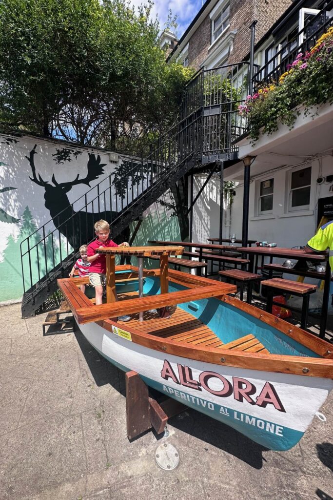 Two young boys playing in a wooden boat converted into pub garden seating in Richmond London