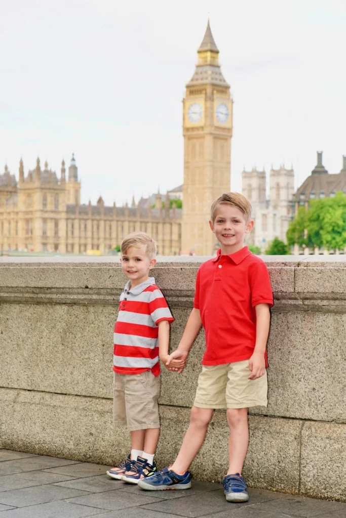 Two young brothers holding hands in front of Big Ben and the Houses of Parliament in London.