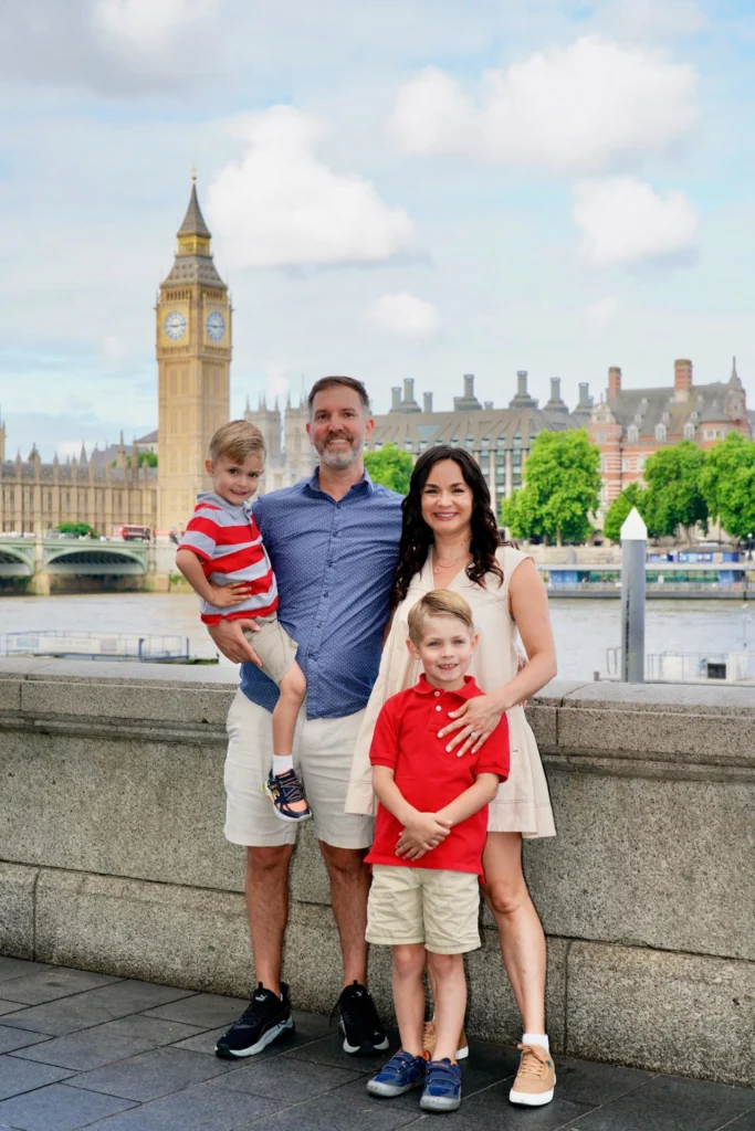 Family of four posing by the Thames with Big Ben and Westminster behind them on a summer day.