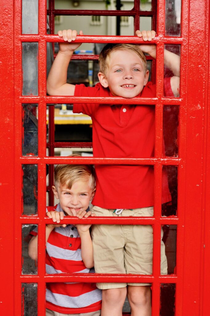 Two boys looking out through the window of a red London telephone box.