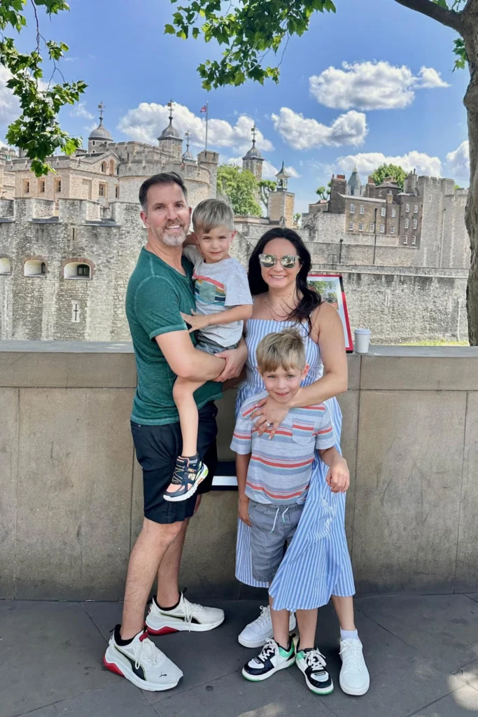 Family of four in front of the stone walls of the Tower of London on a sunny day.