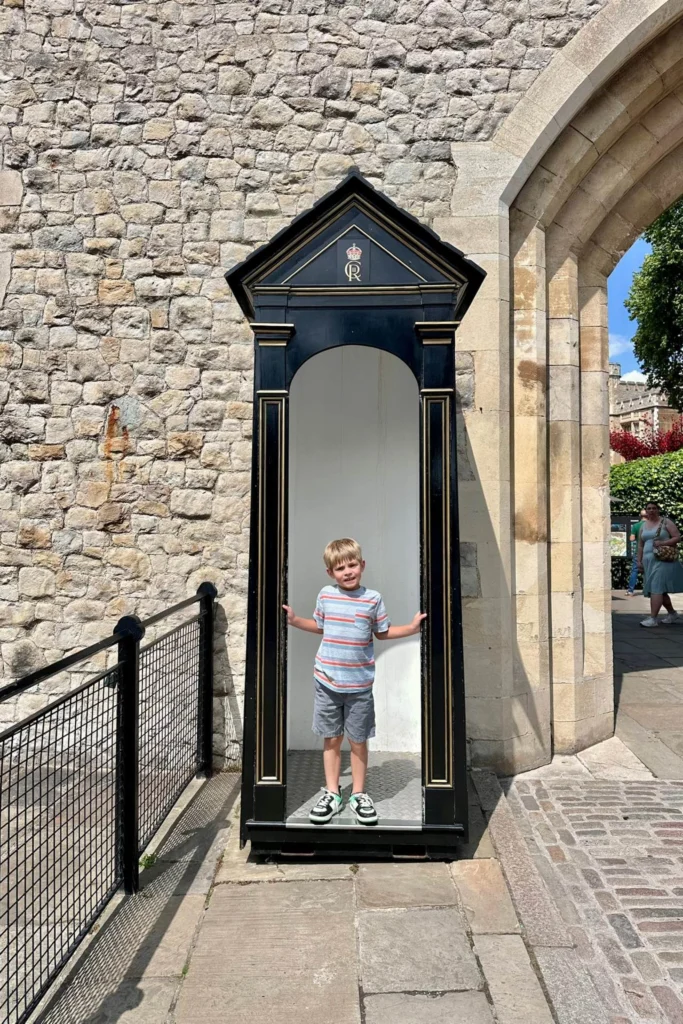 Young boy standing inside a black sentry box at the Tower of London.