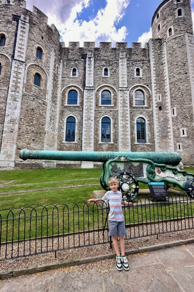 Boy standing in front of an ornate green cannon outside the White Tower at the Tower of London.