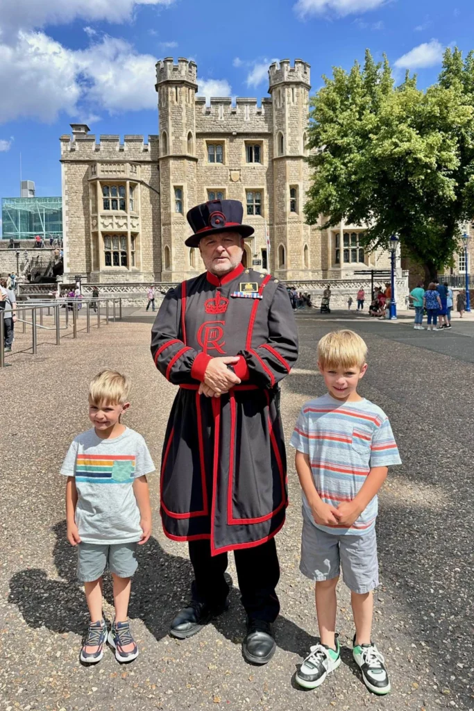Two boys standing with a Yeoman Warder in uniform at the Tower of London.