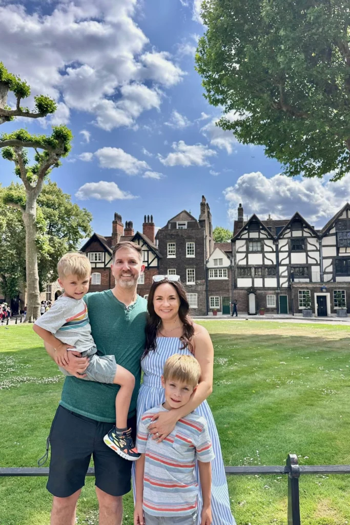Family of four on the green inside the Tower of London with Tudor buildings behind them.