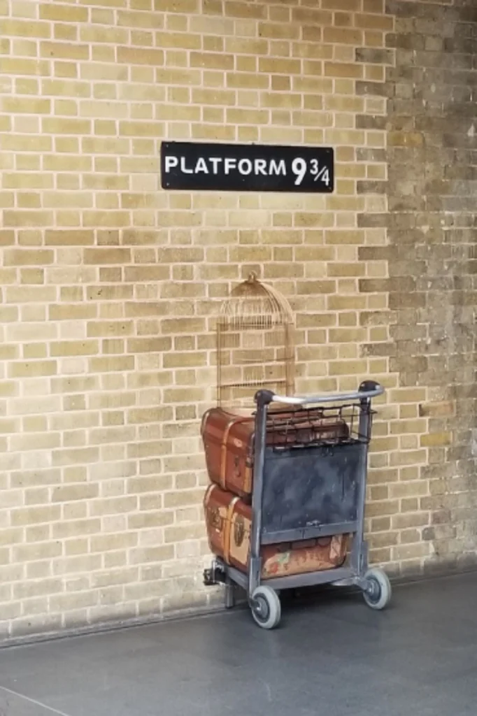 Luggage trolley disappearing into the wall beneath the Platform 9¾ sign at King's Cross station.