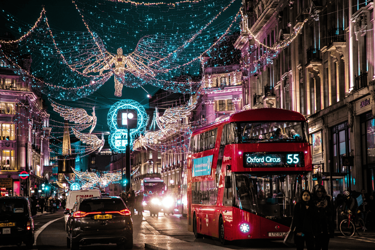 Illuminated angel lights arching over Regent Street at night with a red double decker bus passing underneath. Things to do in london