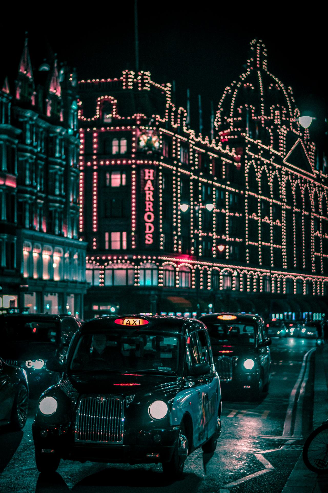 Harrods covered in thousands of lights at night with black taxis lined up on the street in front.