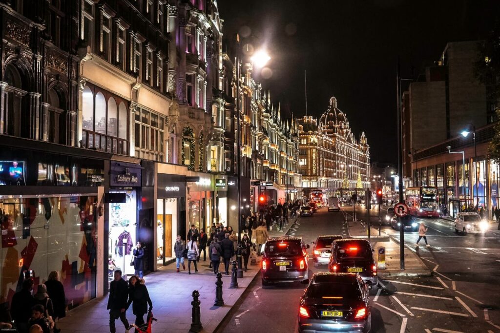 Brompton Road at night during Christmas in London, with shop windows lit and Harrods glowing in the distance.