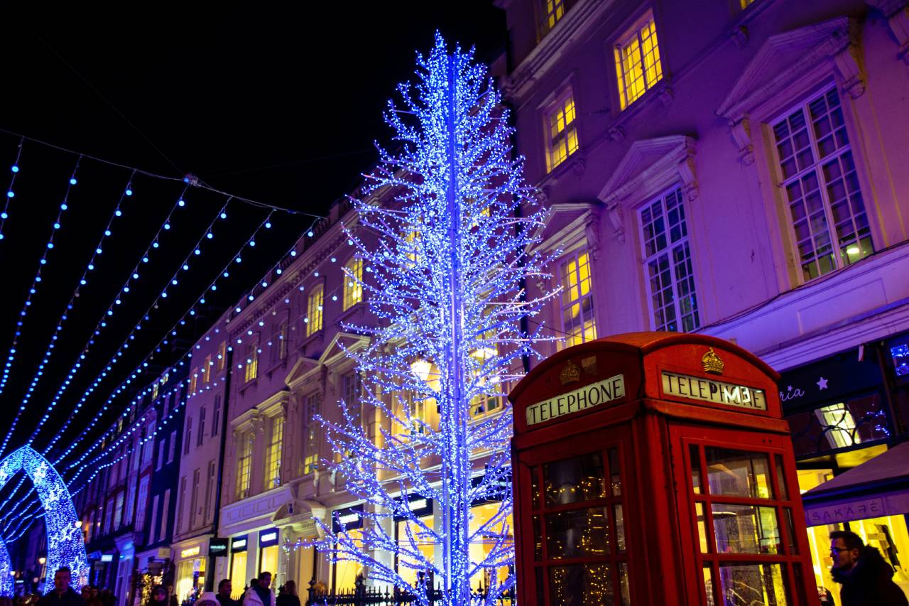 Tree covered in blue lights beside a red telephone box on a London street decorated for Christmas.