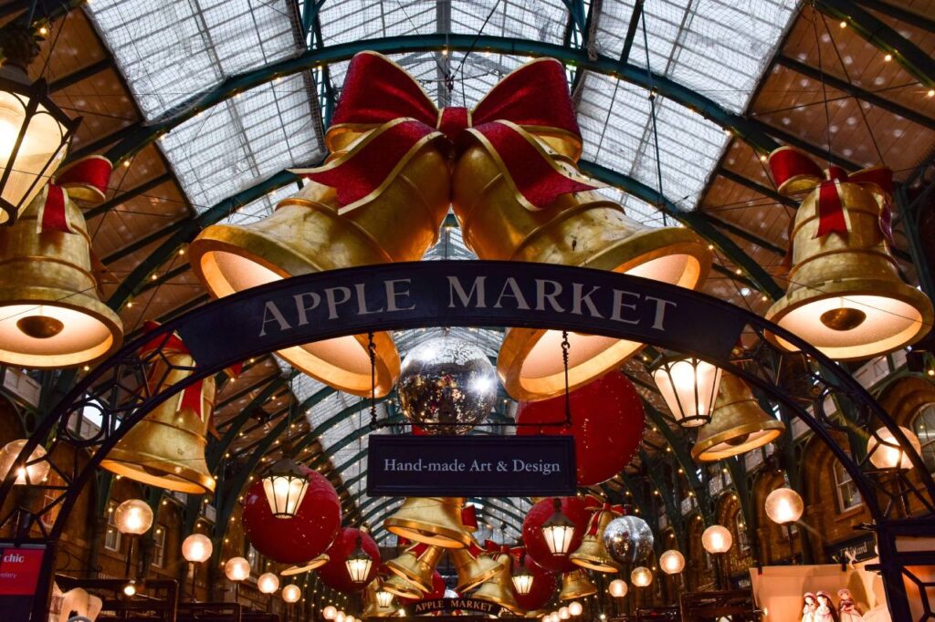 Giant gold bells and red bows hanging above the Apple Market sign in Covent Garden at Christmas.