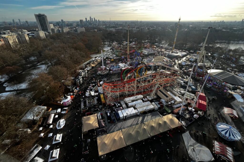 Aerial view of Hyde Park Winter Wonderland showing the rollercoaster, rides and market stalls with the London skyline behind.