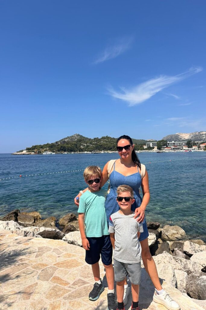 Mom and her two sons on a rocky waterfront with clear blue Adriatic water and a green headland behind them