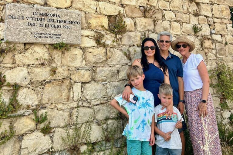 Three generations of a family standing by the 1930 earthquake memorial plaque on an old stone wall in Aquilonia