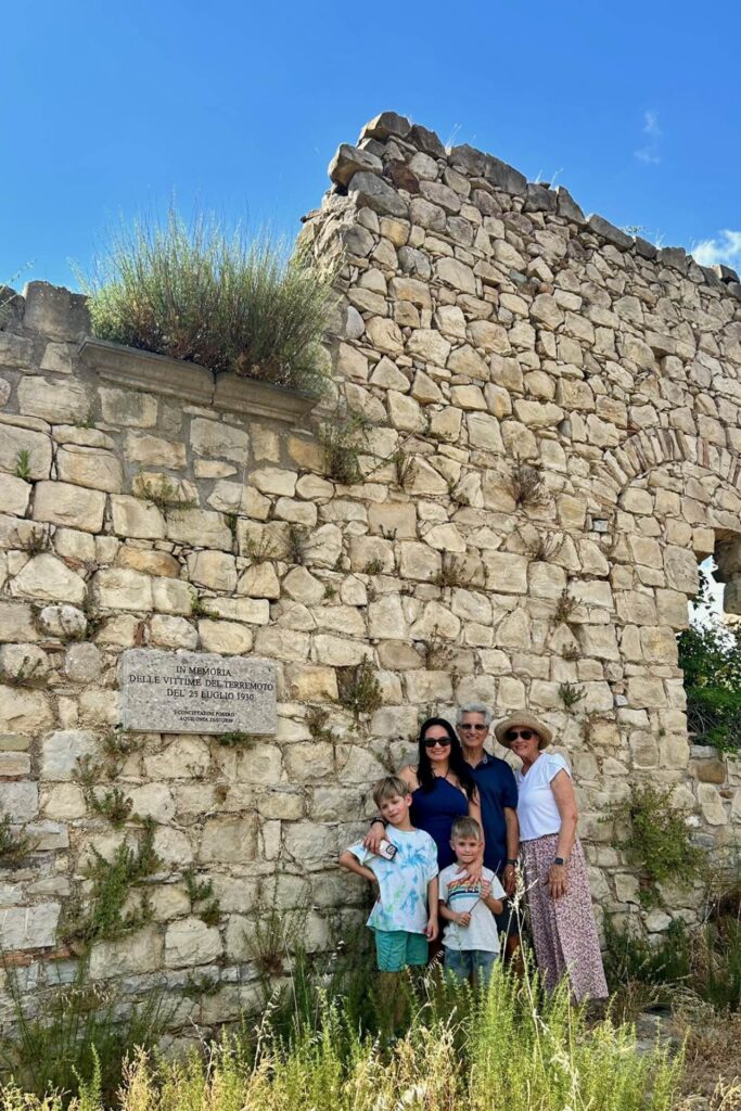 Mari, her sons and her parents at the base of a crumbling stone wall in Aquilonia under a bright blue sky, on their family roots trip